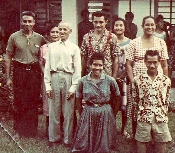 Family photograph from 1964 taken outside a house in Samoa as Foalima left on his mission, with family members standing and kneeling on the grass.